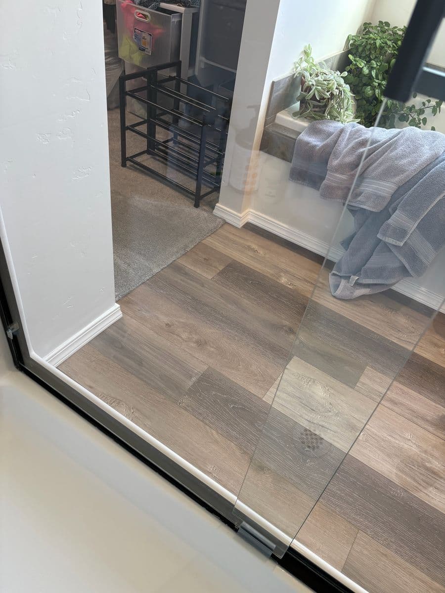Clear shower glass after cleaning, towels and wood floor sharply visible through the glass
