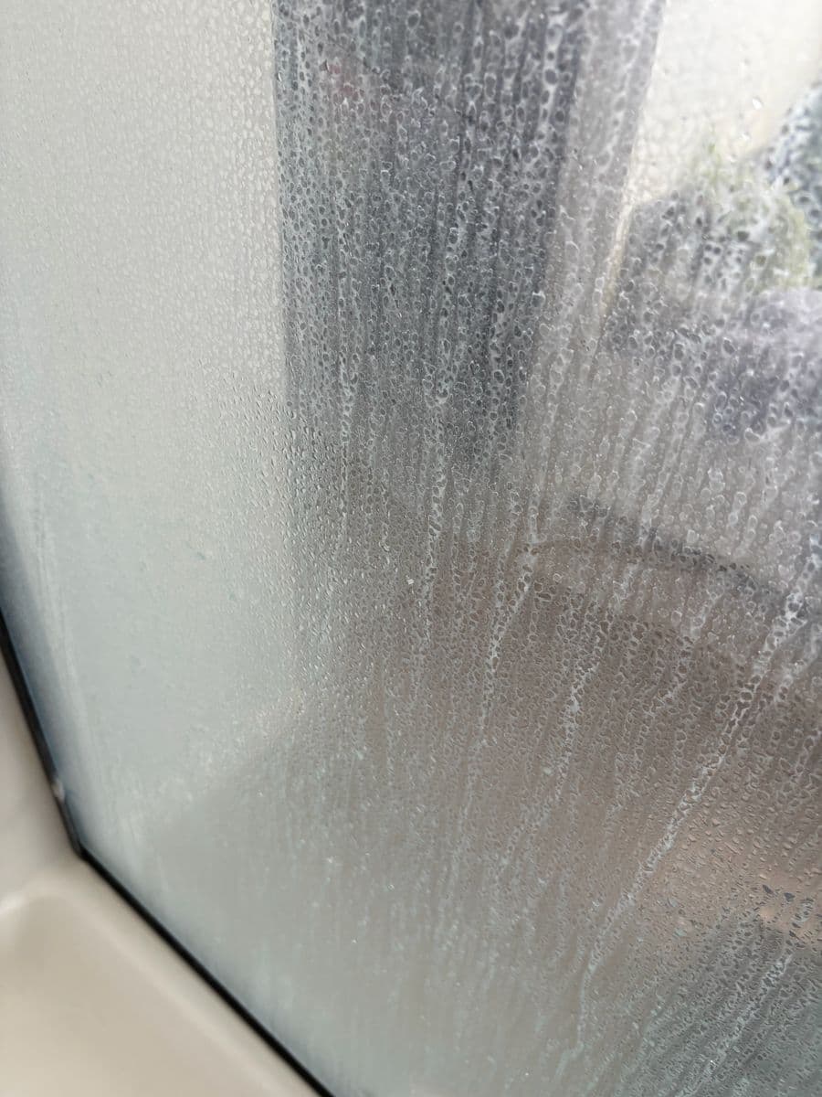 Close-up of shower glass before cleaning, covered in heavy hard-water spots and streaks