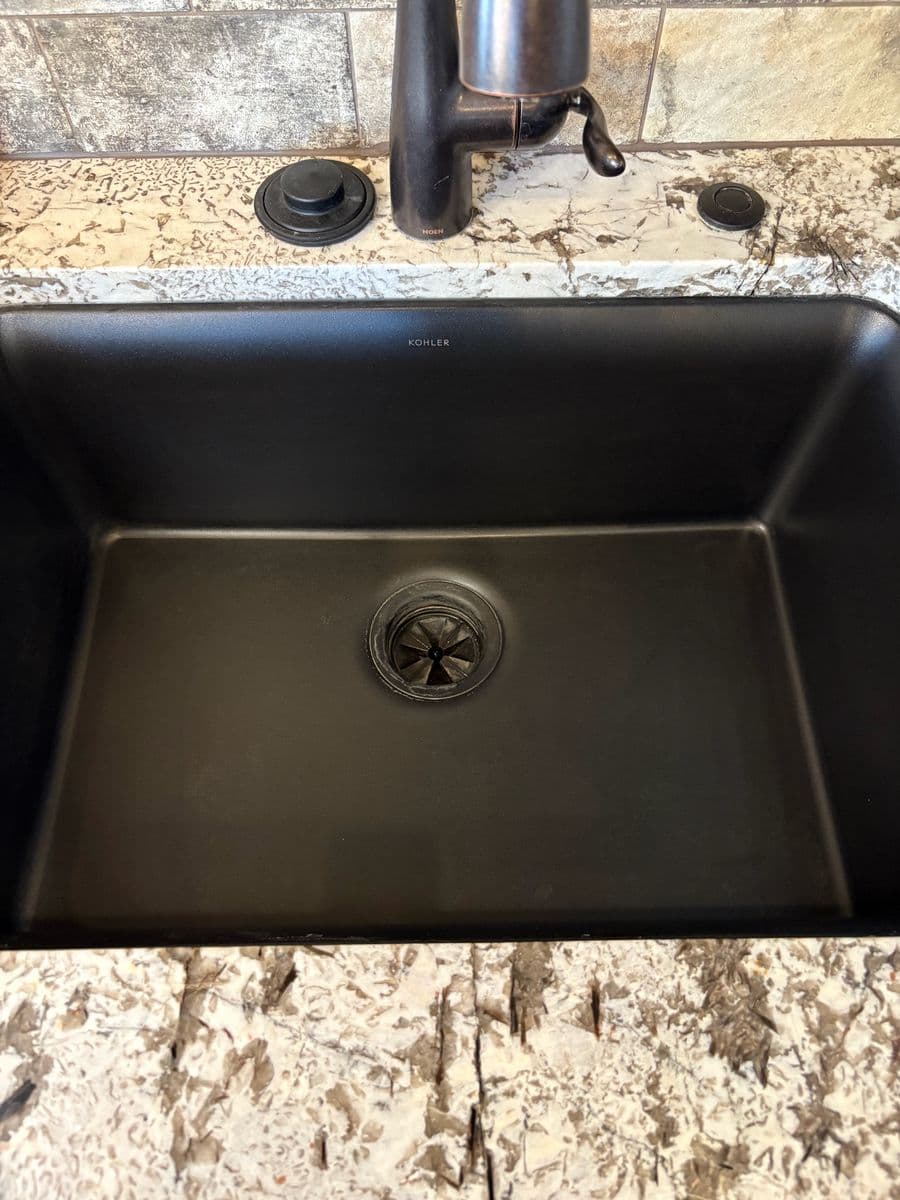 Same black composite kitchen sink after cleaning, basin a clean, even matte black with mineral buildup removed