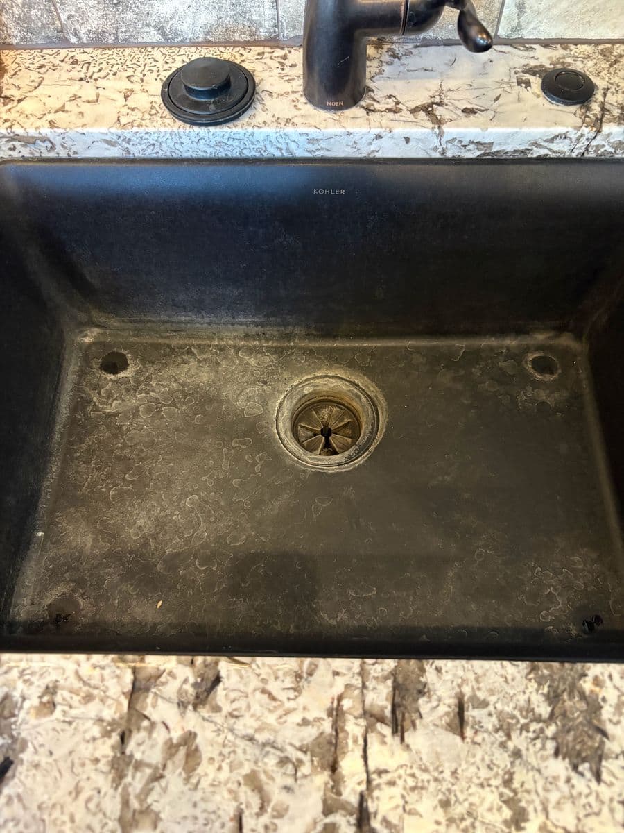 Black composite kitchen sink before cleaning, basin coated in white hard-water and mineral buildup