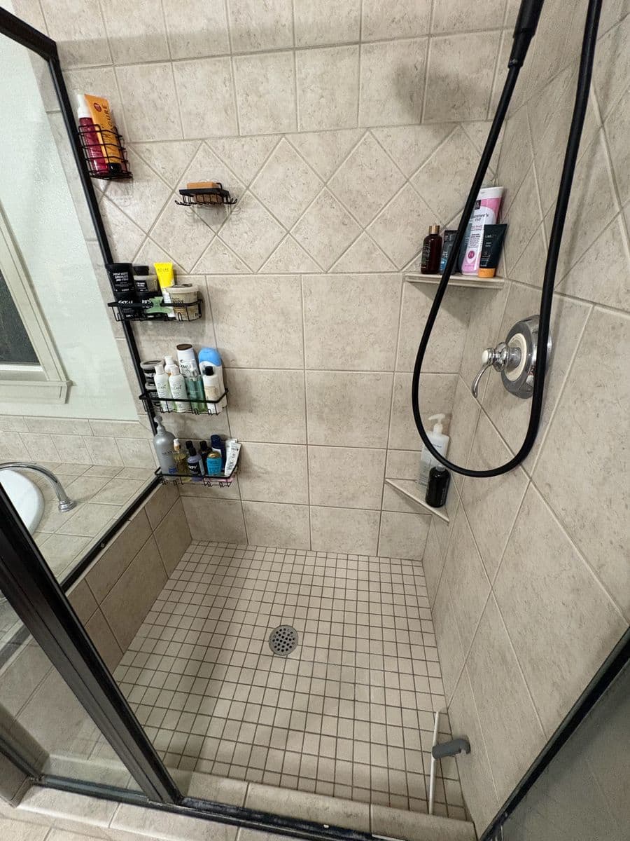 Same walk-in shower after cleaning, beige diagonal wall tile and square floor tile bright and clean behind black-framed glass